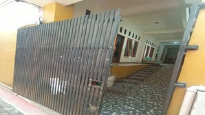 Une entrée fermée par un portail en métal, un chemin dallé menant à un bâtiment à la façade jaune et un escalier.