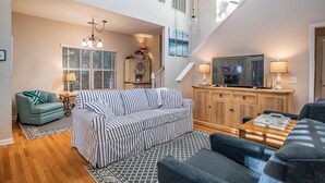 Ein geräumiges Wohnzimmer mit einem gestreiften Sofa, einem blauen Sessel und einem Holzkabinett.