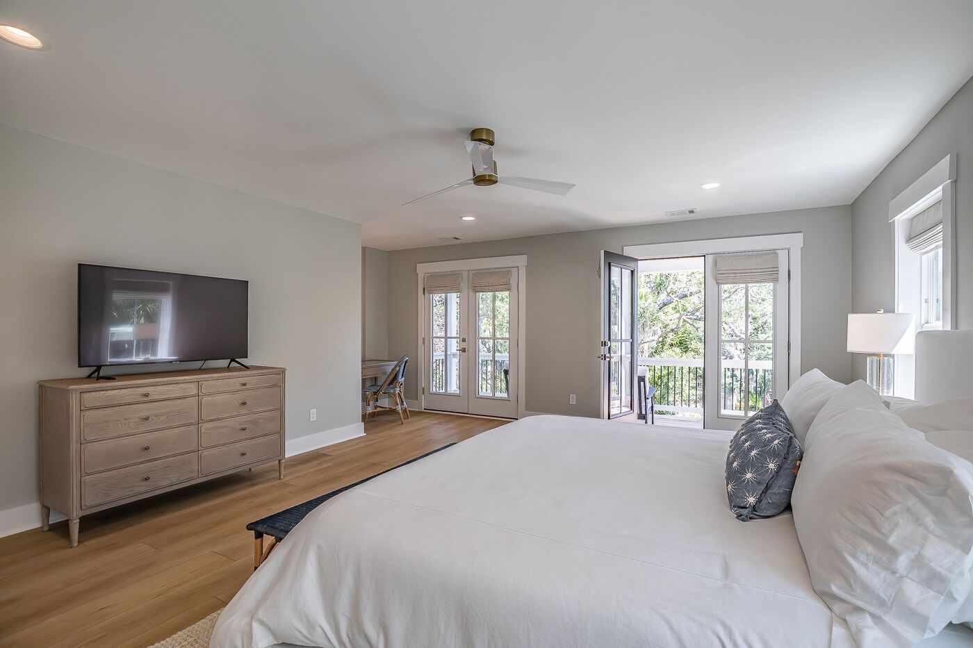 A bedroom with a large bed, a TV on a dresser, and a balcony with glass doors.