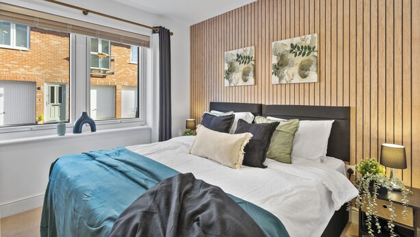 Une chambre moderne avec un grand lit, un mur recouvert de panneaux en bois et des œuvres d’art.