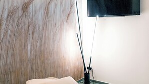 Un dormitorio moderno con un televisor grande montado en la pared, una cama con cubierta blanca texturizada y un panel decorativo.