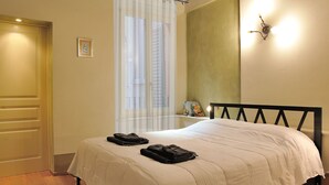 A bedroom with a wooden ceiling, a bed with white bedding, a window with blinds, and a wall-mounted light fixture. - Orfeo's House (Modena)