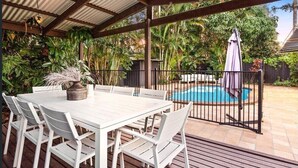 Un patio abrité avec une piscine, des meubles blancs et une végétation luxuriante.
