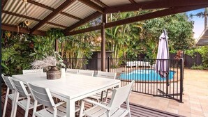 Terrassa exterior amb taula i cadires blanques, una piscina i vegetació exuberant.