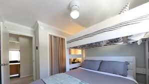 Un dormitorio con una cama individual superpuesta, una mesita de noche con lámpara, una ventana con cortinas y un ventilador de techo.