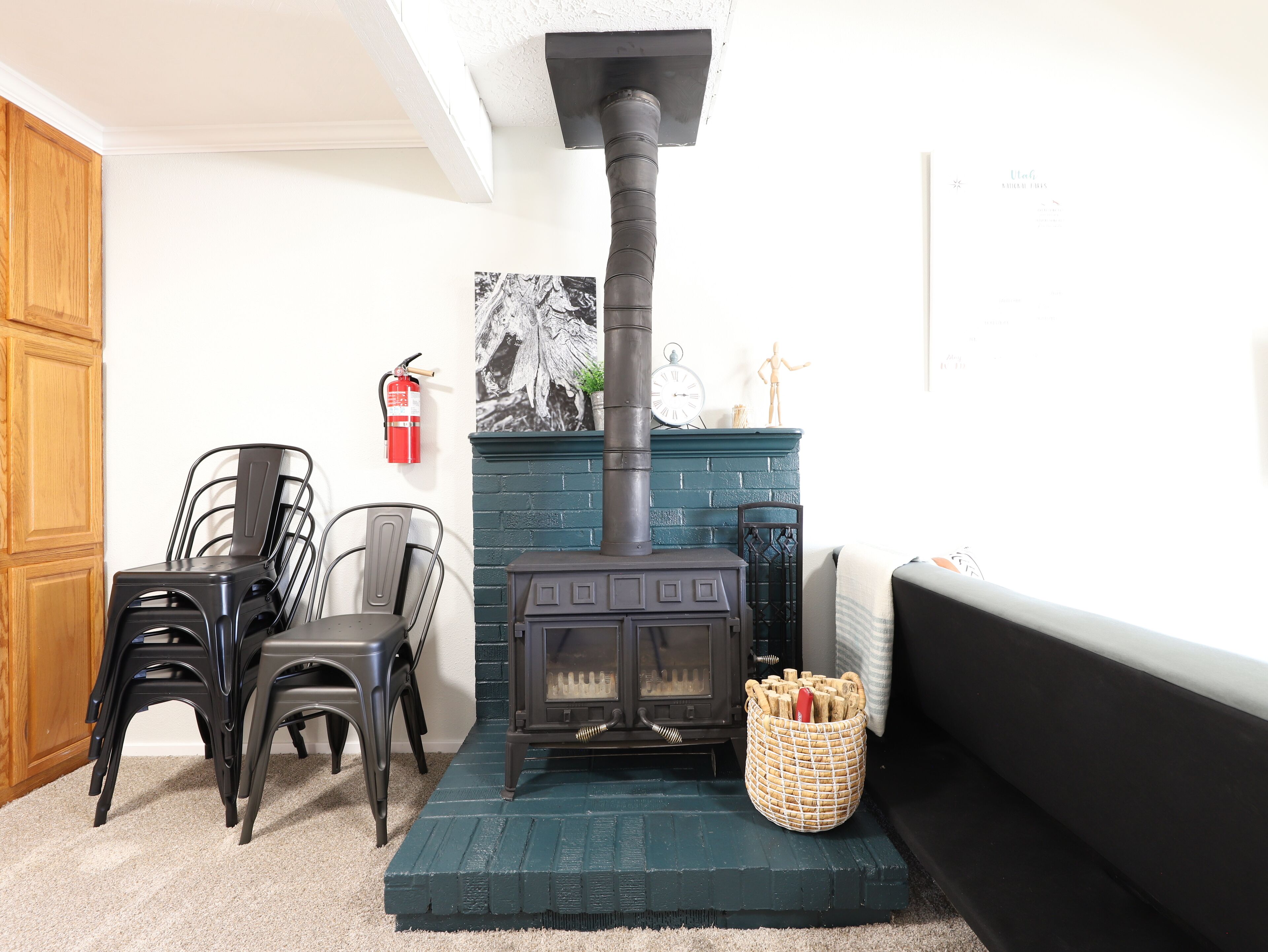 Um quarto aconchegante com uma lareira a lenha preta, uma mesa de jantar com cadeiras, um extintor de incêndio e um objeto decorativo na parede.