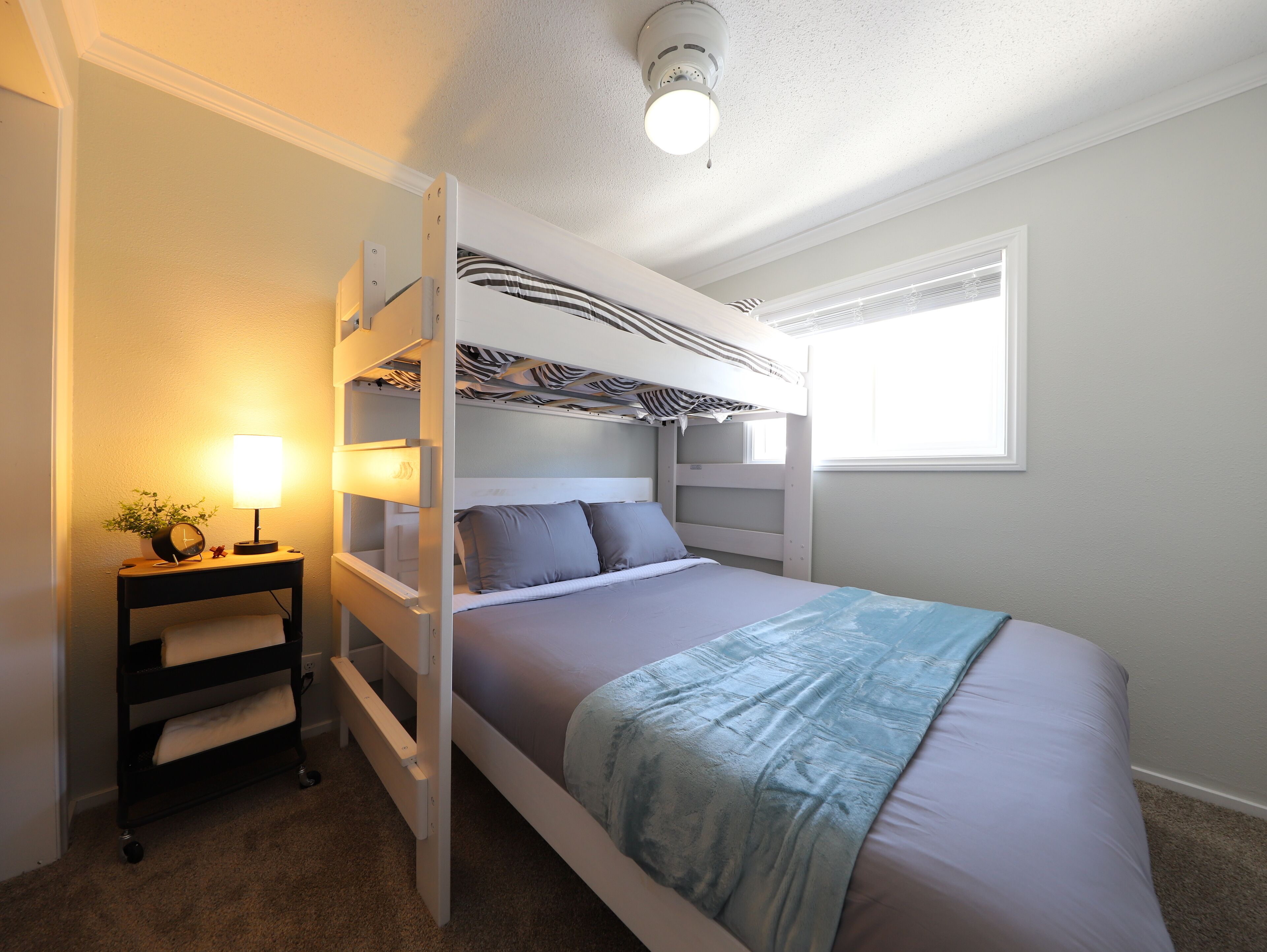 A bunk bed with a zebra-patterned headboard, a bedside table with a lamp, and a window with blinds.