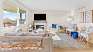 A spacious living room with a fireplace, comfortable seating, a television, and a view of the outdoors. - Boho Hillside Retreat In Boises Northend (Boise)