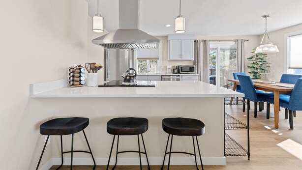 A modern kitchen with a central island, bar stools, and a dining area with blue chairs. - Boho Hillside Retreat In Boises Northend (Boise)