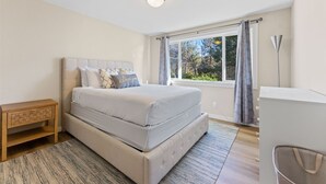 A bedroom with a large bed, a bedside table, a desk, and a window with curtains. - Boho Hillside Retreat In Boises Northend (Boise)