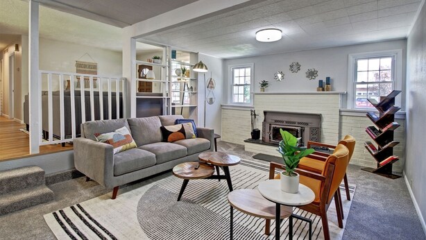 A spacious living room with a grey sofa, a fireplace, a staircase, and a bookshelf.