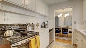 A modern kitchen with white cabinets, a stainless steel stove, and a dining area with a chandelier.