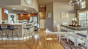 A modern kitchen with wooden cabinets, a central island with bar stools, a dining area with a chandelier, and a clock on the wall. - Dog Friendly Cozy Quiet Eagle ID Home sleeps 6 (Eagle)