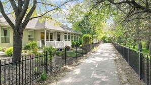 A residential street with a house featuring a porch and a fenced yard. - Luxury Picturesque Home On The Greenbelt (Garden City)