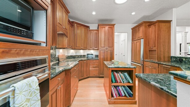 A kitchen with wooden cabinets, granite countertops, a built-in bookshelf, and stainless steel appliances. - Luxury Picturesque Home On The Greenbelt (Garden City)
