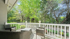 A covered outdoor deck with wicker furniture and a white railing. - Luxury Picturesque Home On The Greenbelt (Garden City)