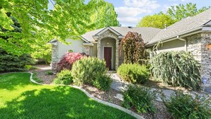 A residential house with a stone facade, a red door, and a well-maintained garden with various shrubs and a lawn. - Luxury Picturesque Home On The Greenbelt (Garden City)