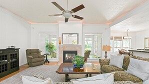 A spacious living room with a fireplace, a ceiling fan, and a view of the outdoors. - Luxury Picturesque Home On The Greenbelt (Garden City)