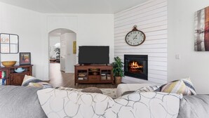 Uma sala de estar com lareira, uma televisão sobre um suporte de madeira e um relógio grande na parede.