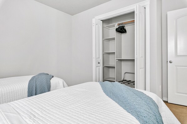 A bedroom with two beds, a closet with hanging space, and a door.