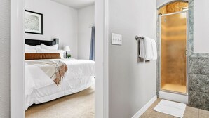 Une chambre avec un lit, une table de chevet et un tableau accroché au mur. La pièce a un mur blanc et un sol recouvert de moquette.