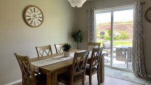 Ein Essbereich mit Holztisch und -stühlen, einer Wanduhr, einem Blumentopf und Blick durch eine Glastür.