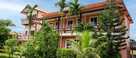 A multi-story building with a red-tiled roof, surrounded by lush greenery and palm trees.