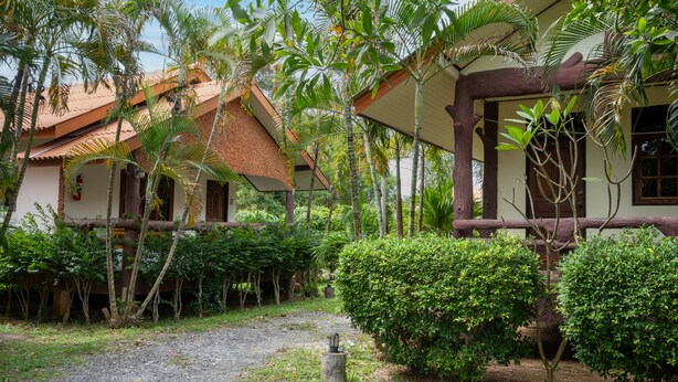 A traditional house with a thatched roof, surrounded by lush greenery and a gravel path. - Lanta School Beach Resort (Ko Lanta)