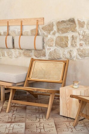 A wooden chair with a woven backrest, a cushioned bench, and a small wooden table with a candle. - ERAMAI (Patras)