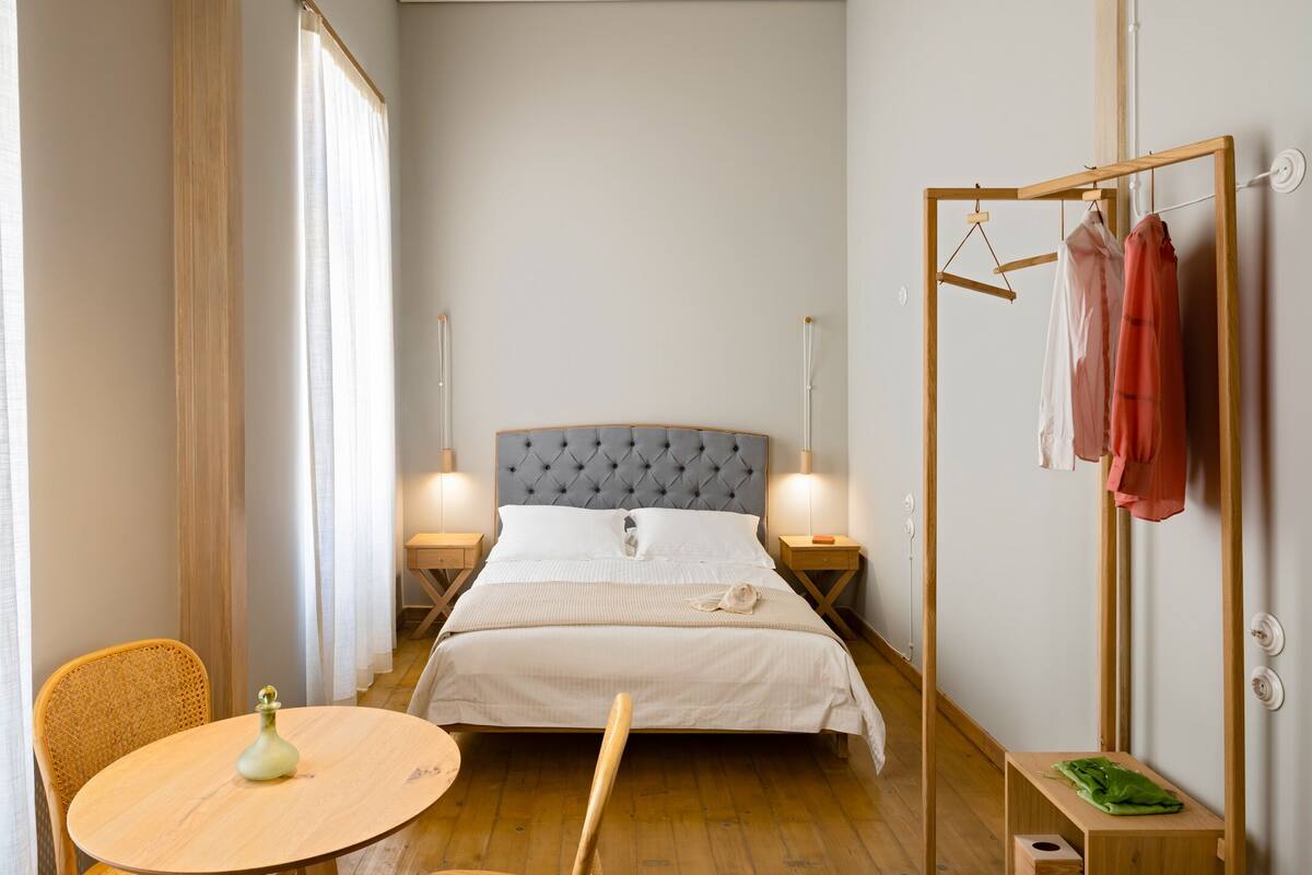 Ein Schlafzimmer mit einem Bett, Nachttischen, einem Sessel, einem Tisch und einem Kleiderständer.