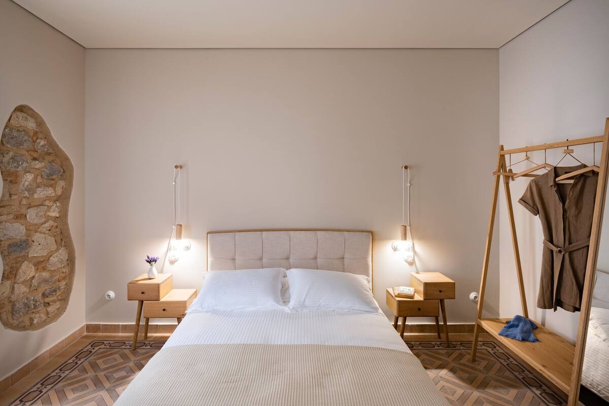 Ein ordentlich eingerichtetes Schlafzimmer mit einem großen Bett, Nachttischen, einem Kleiderhaken und einer Wand aus Stein.