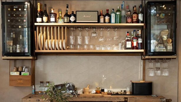Eine Bar mit Regalen voller Spirituosenflaschen, Gläsern und einem alten Smeg-Kühlschrank.