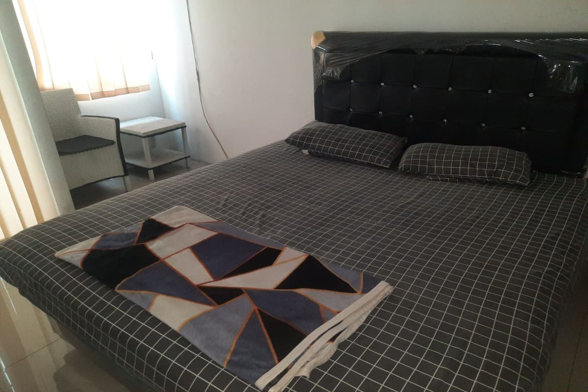 A neatly made bed with a geometric-patterned blanket, a black upholstered headboard, and two pillows.