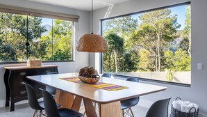 A modern dining area with a large table, black chairs, and a hanging light fixture.