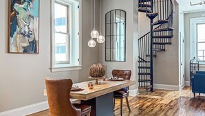 A spacious dining area with a wooden table and chairs, a modern chandelier, and a spiral staircase. - The Historic Lyric Penthouse with Private Rooftop (Cincinnati)
