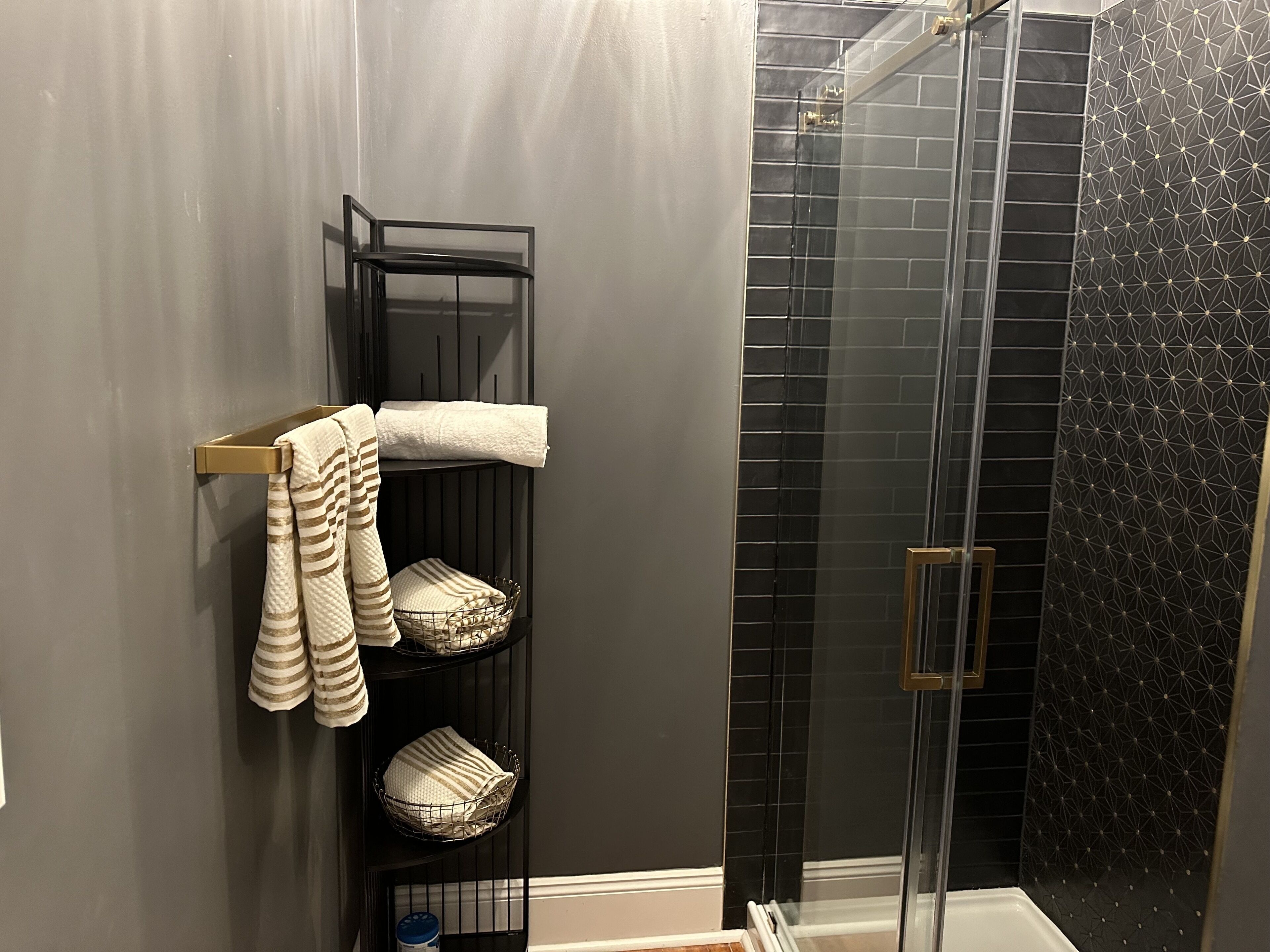 Een badkamer met een glazen douchecabine, een handdoekrek met gestreepte handdoeken en een wand betegeld met zwart tegelwerk.