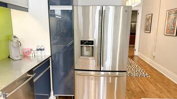 A stainless steel refrigerator with a water dispenser, a coffee maker, and a microwave on a wooden floor with a patterned rug.