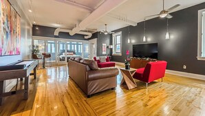 A spacious living room with hardwood floors, a large sofa, a red armchair, a coffee table, and a flat-screen TV mounted on the wall. - The Historic Lyric Penthouse with Private Rooftop (Cincinnati)
