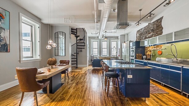 A modern kitchen with a central island, a dining area with a wooden table and chairs, and a spiral staircase leading to an upper level. - The Historic Lyric Penthouse with Private Rooftop (Cincinnati)