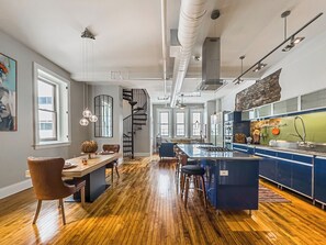 A modern kitchen with a central island, a dining area with a wooden table and chairs, and a spiral staircase leading to an upper level. - The Historic Lyric Penthouse with Private Rooftop (Cincinnati)