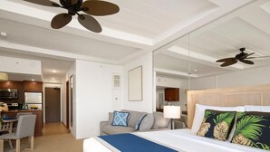 A hotel room with a bed, a desk, a kitchenette, and a ceiling fan. - Whaler | Ocean View Studio Sleeps 4 | Car Incl. w/ 6+ Nights | WH2-661 by KBM (Lahaina)