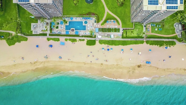 An aerial view of a resort with a large pool, beach, and high-rise buildings. - Whaler | Ocean View Studio Sleeps 4 | Car Incl. w/ 6+ Nights | WH2-661 by KBM (Lahaina)