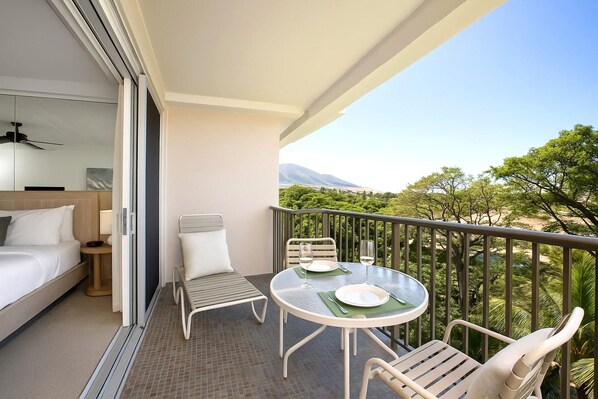 A balcony with a bed, a table with chairs, and a view of a mountainous landscape.