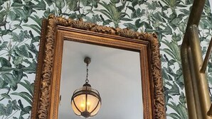 A mirror with an ornate gold frame on a wall with a leafy wallpaper pattern. - Opening Doors Premià Dalt Amazing views with pool (Premià de Dalt)