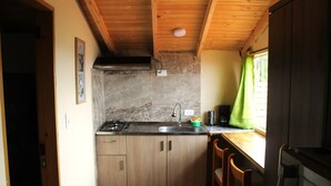 A compact kitchen with wooden cabinets, a sink, and a stove. There is a window with a green curtain, and a trash bin is visible. - Small cozy apartment surrounded by nature in the countryside of Bogotá (Bogotá)