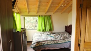 A bedroom with a wooden ceiling, a bed with patterned bedding, a window with green curtains, and a wooden wardrobe. - Small cozy apartment surrounded by nature in the countryside of Bogotá (Bogotá)