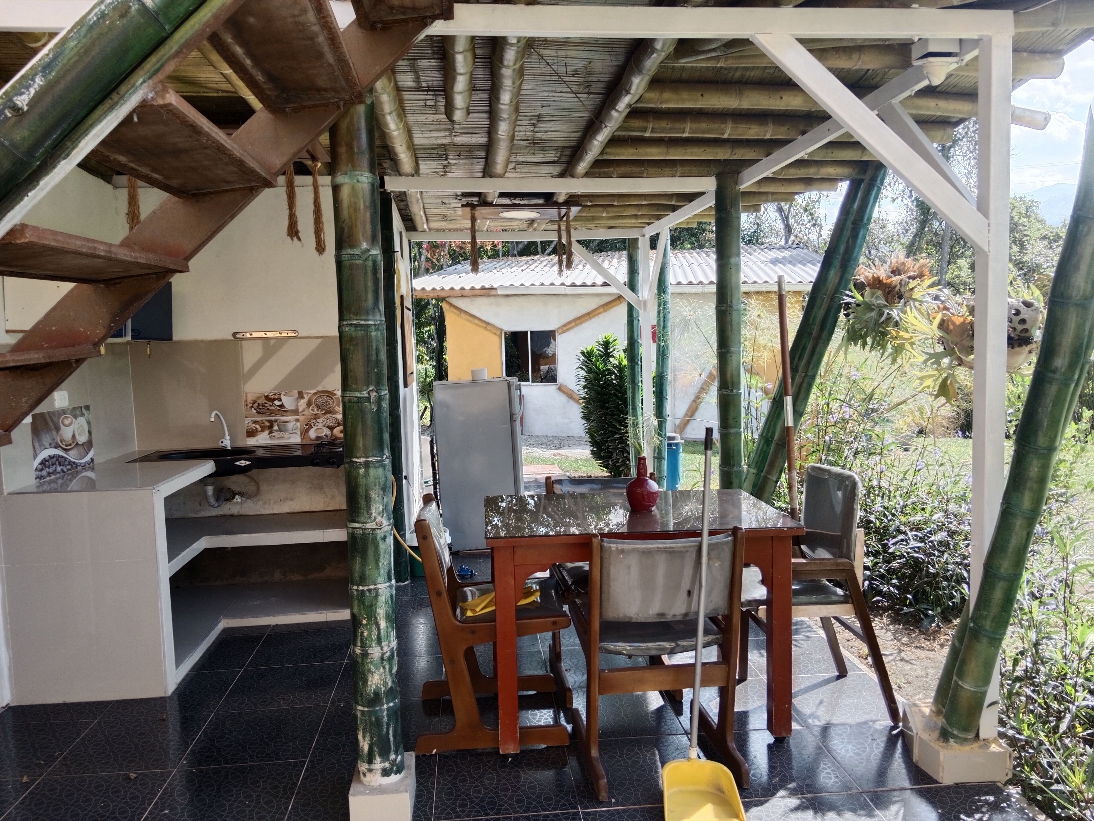 A covered outdoor area with a dining table, chairs, and a kitchen area with a sink and stove.