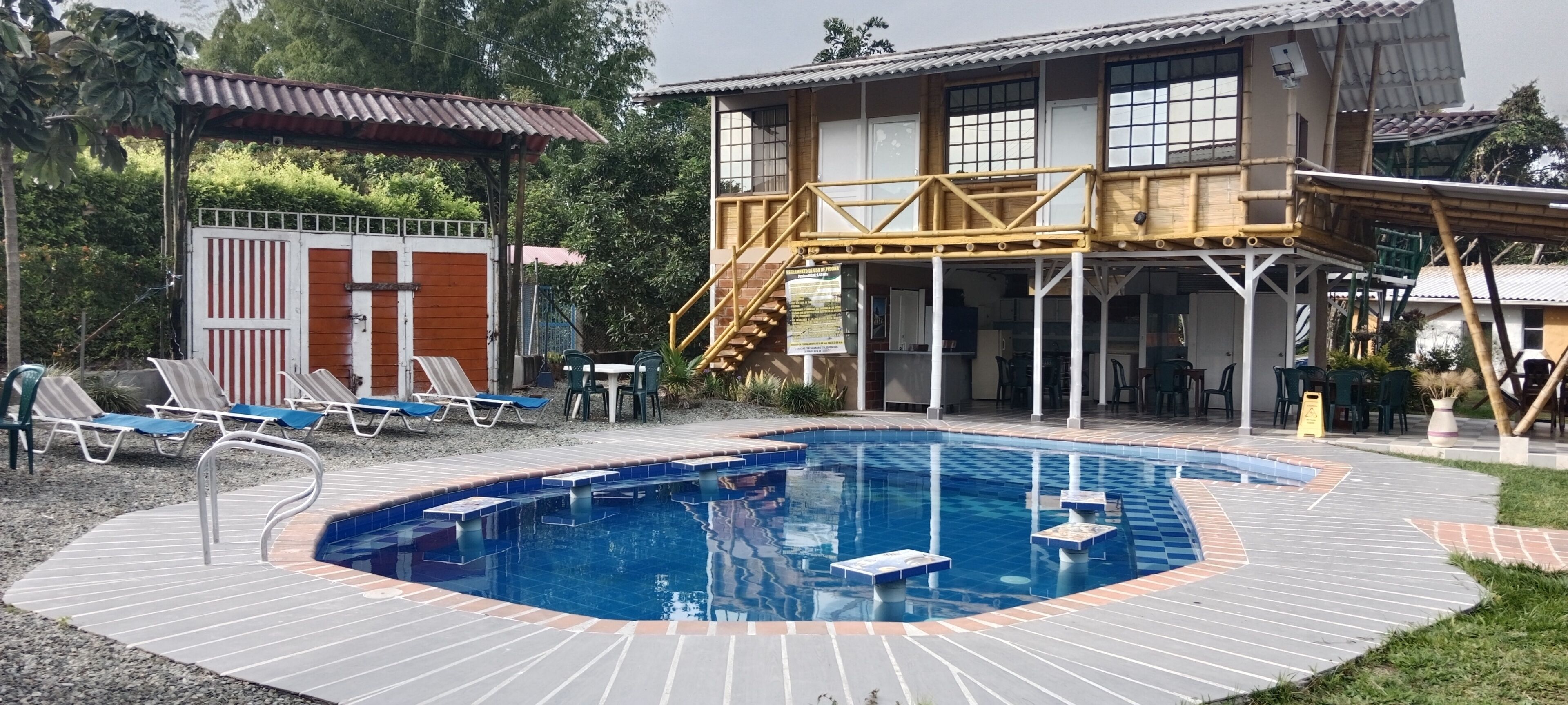 En swimmingpool med ett trädäck, solstolar och en möblerad sittplats under tak.