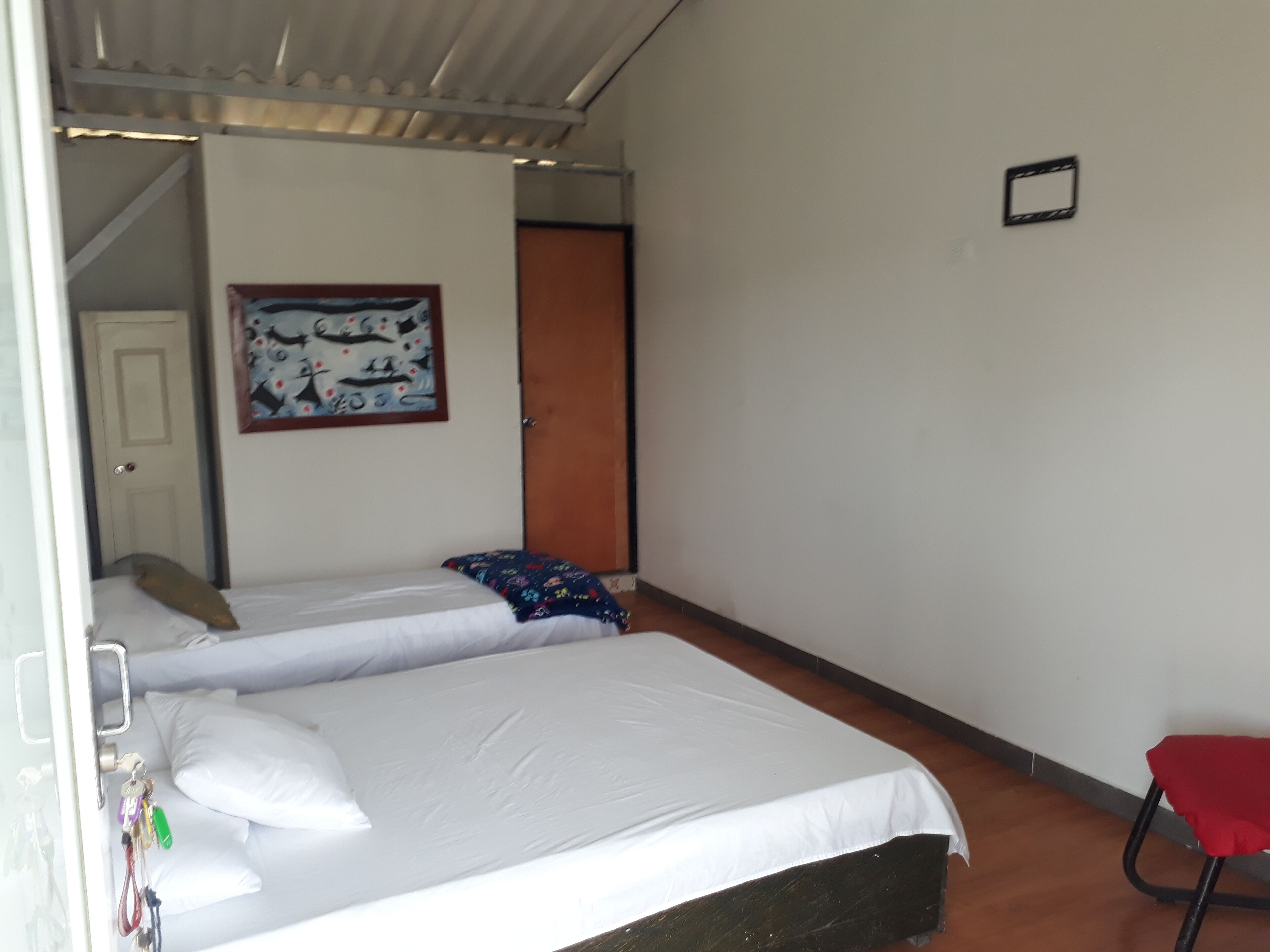 Ein Zimmer mit zwei Einzelbetten, einem roten Sessel, einer Tür und einer Wand mit einem gerahmten Bild.