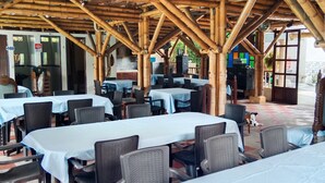 An outdoor restaurant with bamboo structures, tables with white tablecloths, and wicker chairs. - cabañas hotel villa lucia (Calarcá)